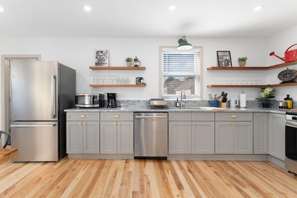 A modern kitchen with grey cabinets, stainless steel appliances, wooden flooring, and built-in shelves with various items. - Fox Point House: Walk to Brown/RISD + Free Parking for Up to 3 Cars! (Providence)