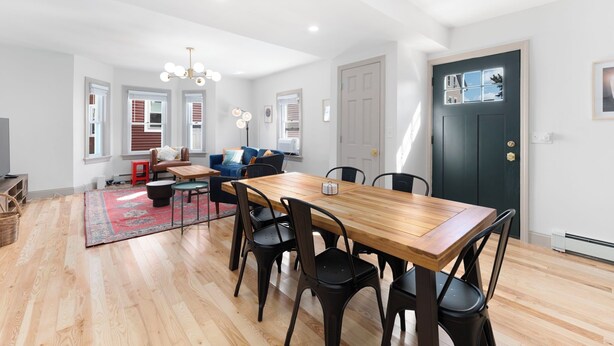 Amplia sala de estar con una mesa de comedor de madera, sillas negras, un tapete rojo y un sofá azul.