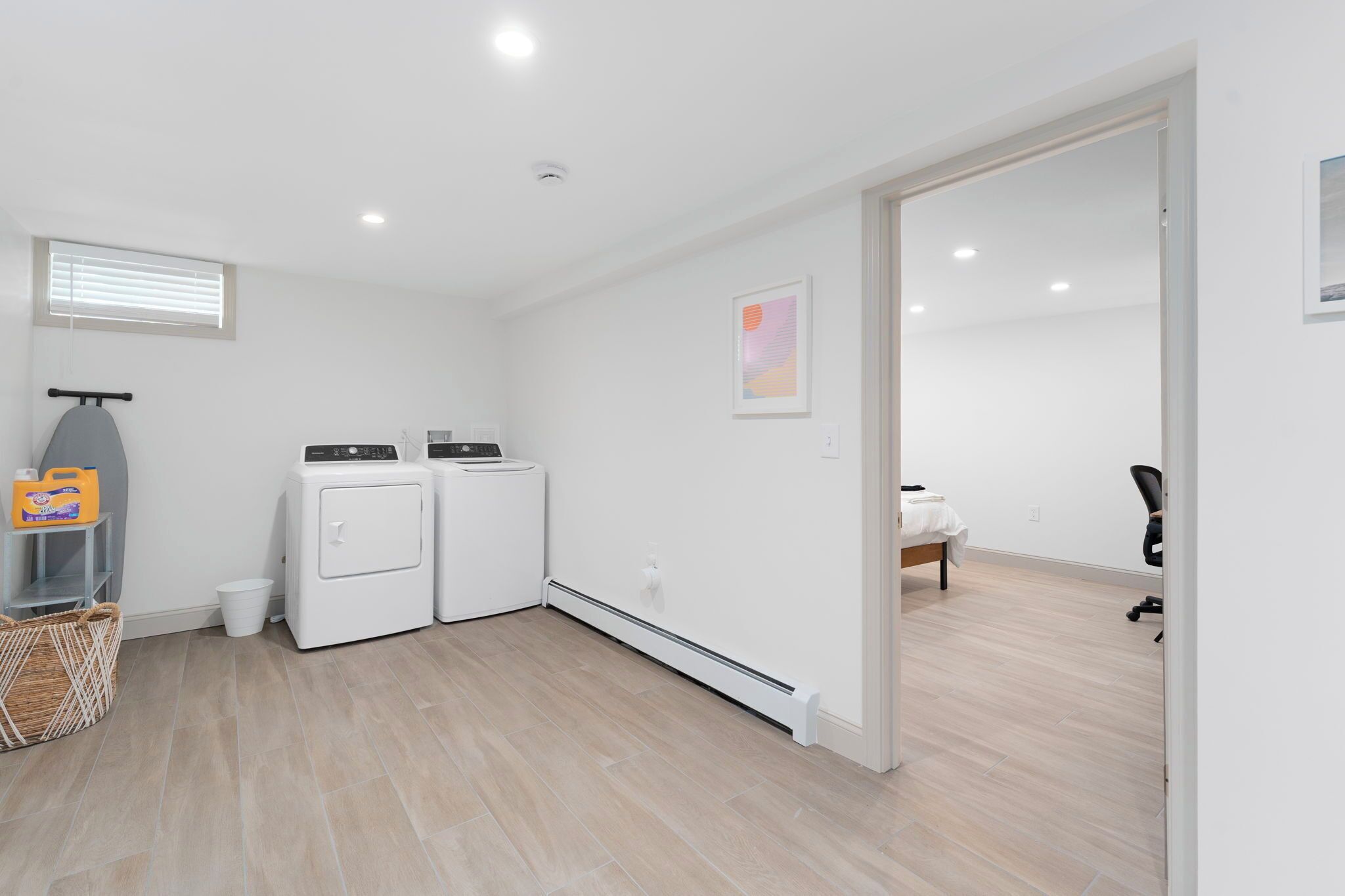 A clean, modern laundry room with two white washing machines, a drying rack, and a basket of laundry supplies.