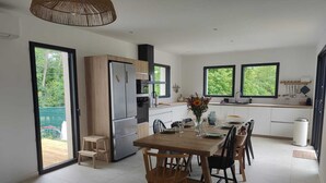 A modern kitchen with a dining area, large windows, and a view of greenery. - Villa in the southern moors, 10 minutes from the ocean (Magescq)