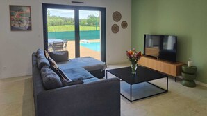 A modern living room with a sofa, a coffee table, a TV, and a view of a swimming pool. - Villa in the southern moors, 10 minutes from the ocean (Magescq)