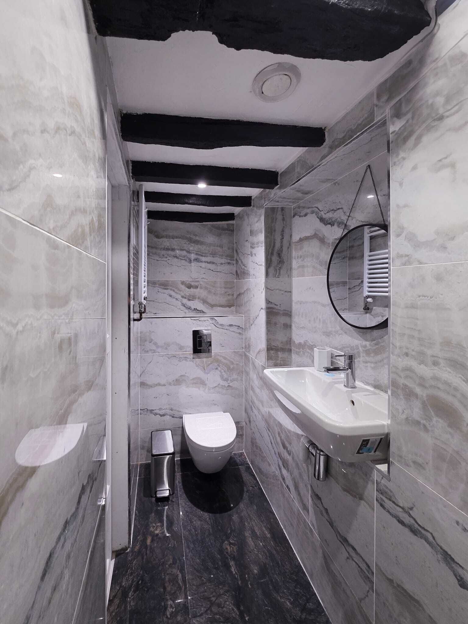 A modern bathroom with a marble floor, a white toilet, a sink, and a mirror.