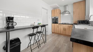 A modern kitchen with white subway tiles, wooden cabinets, a stainless steel range hood, a coffee maker, and a dish rack.
