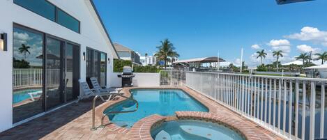 A modern outdoor pool area with a hot tub, lounge chairs, and a view of the surrounding neighborhood.