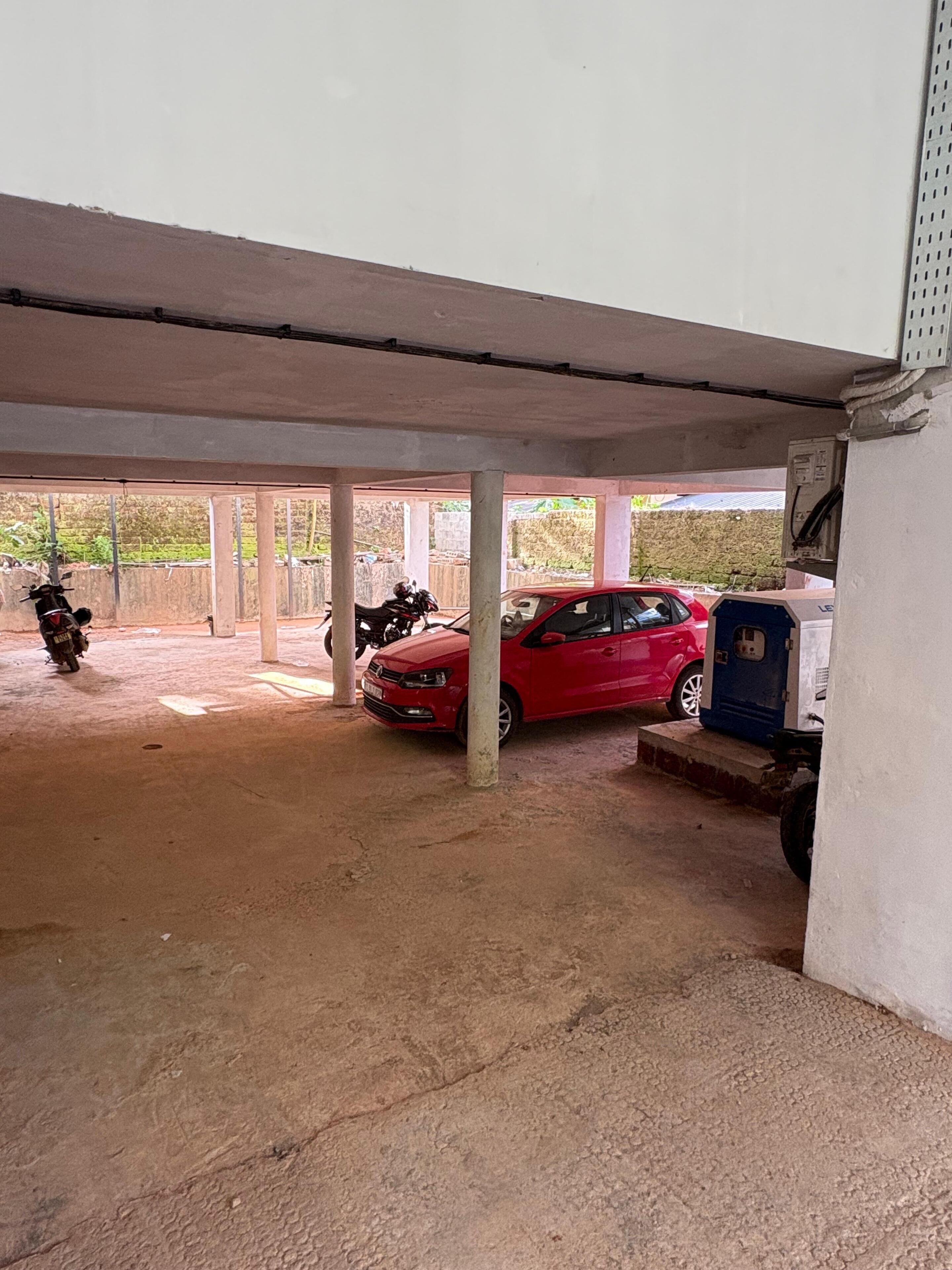 Een overdekte parkeerplaats met een rode auto en een motorfiets, geparkeerd onder een betonnen constructie.