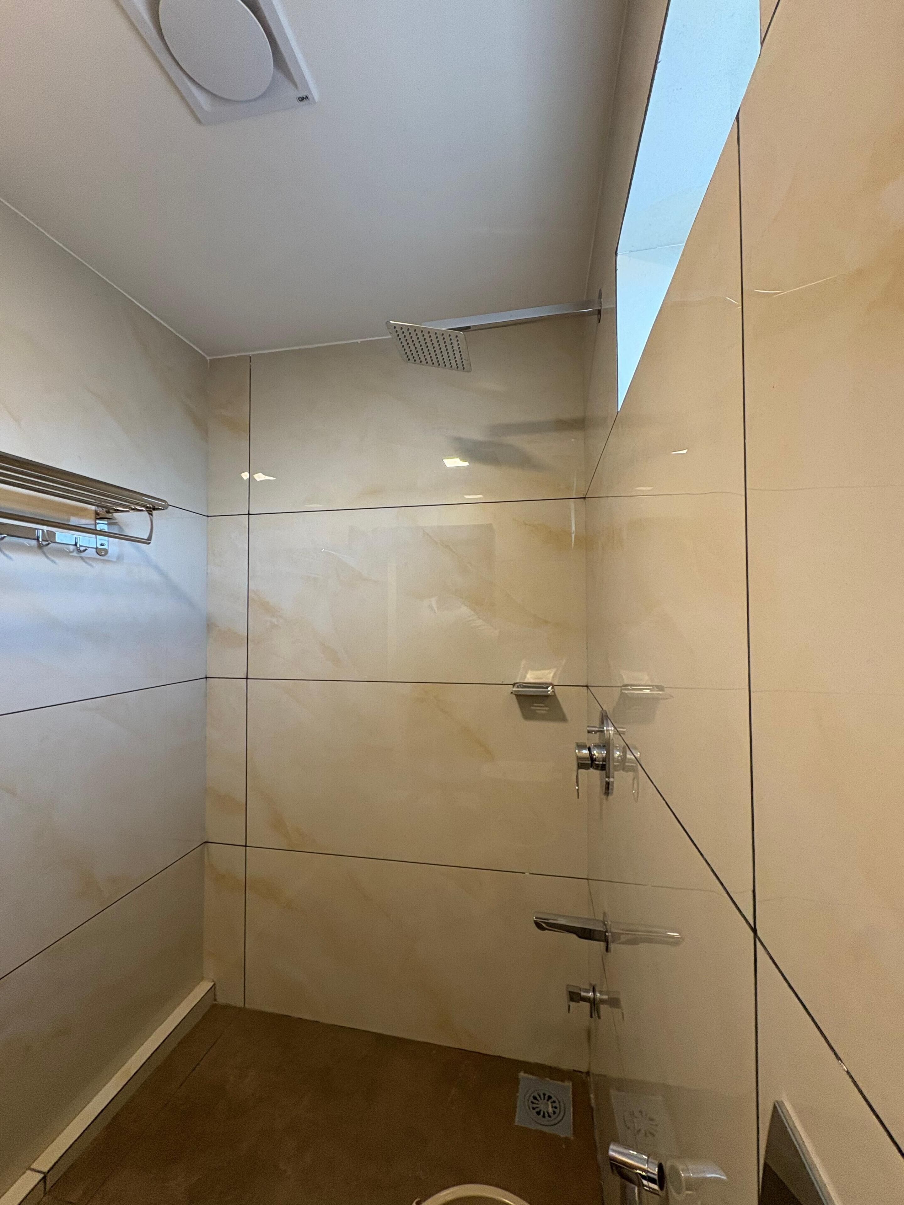 Uma casa de banho moderna com cabine de duche em vidro, um porta-toalhas e um ralo visível.