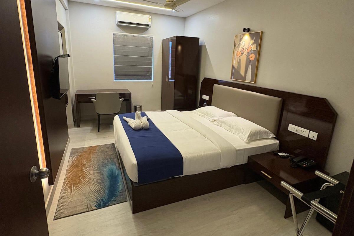 Una habitación de hotel moderna con cama, mesita de noche, escritorio, silla, armario y ventilador de techo.
