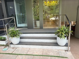 Entrada de hotel con puerta de cristal, una escalera y plantas en macetas.