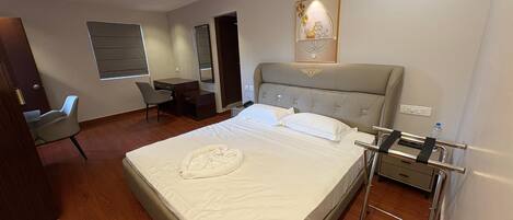 A hotel room with a large bed, a desk, a chair, a mirror, and a wall-mounted artwork.