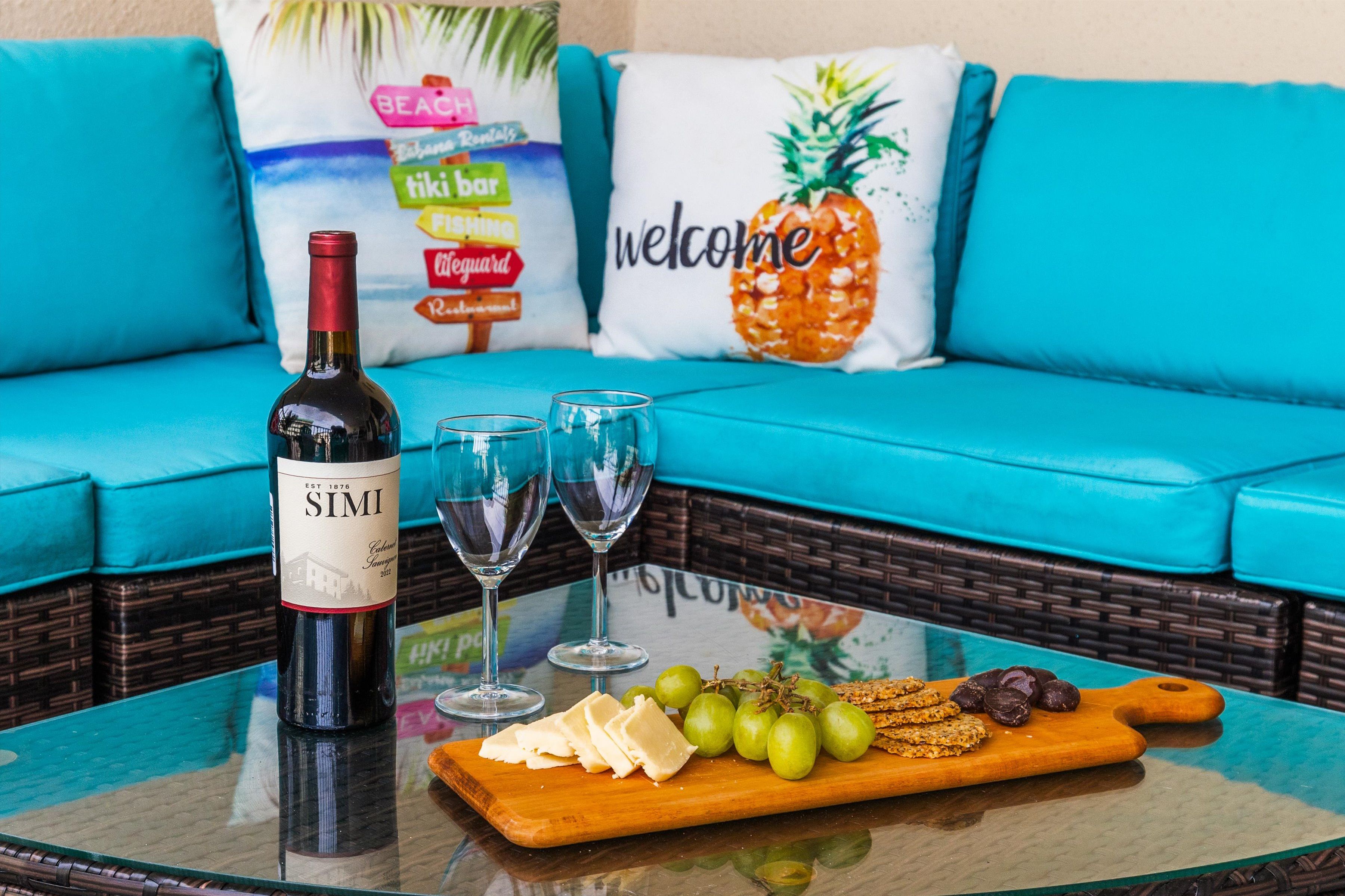 Una botella de vino Simi, dos copas, una tabla de madera con queso, uvas y galletas sobre una mesa de vidrio.