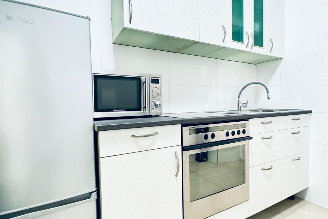 Una cocina con microondas, horno, pileta y muebles blancos.