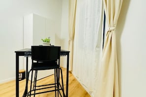 Ett litet rum med en svart stol, ett vitt skåp och en beige gardin.