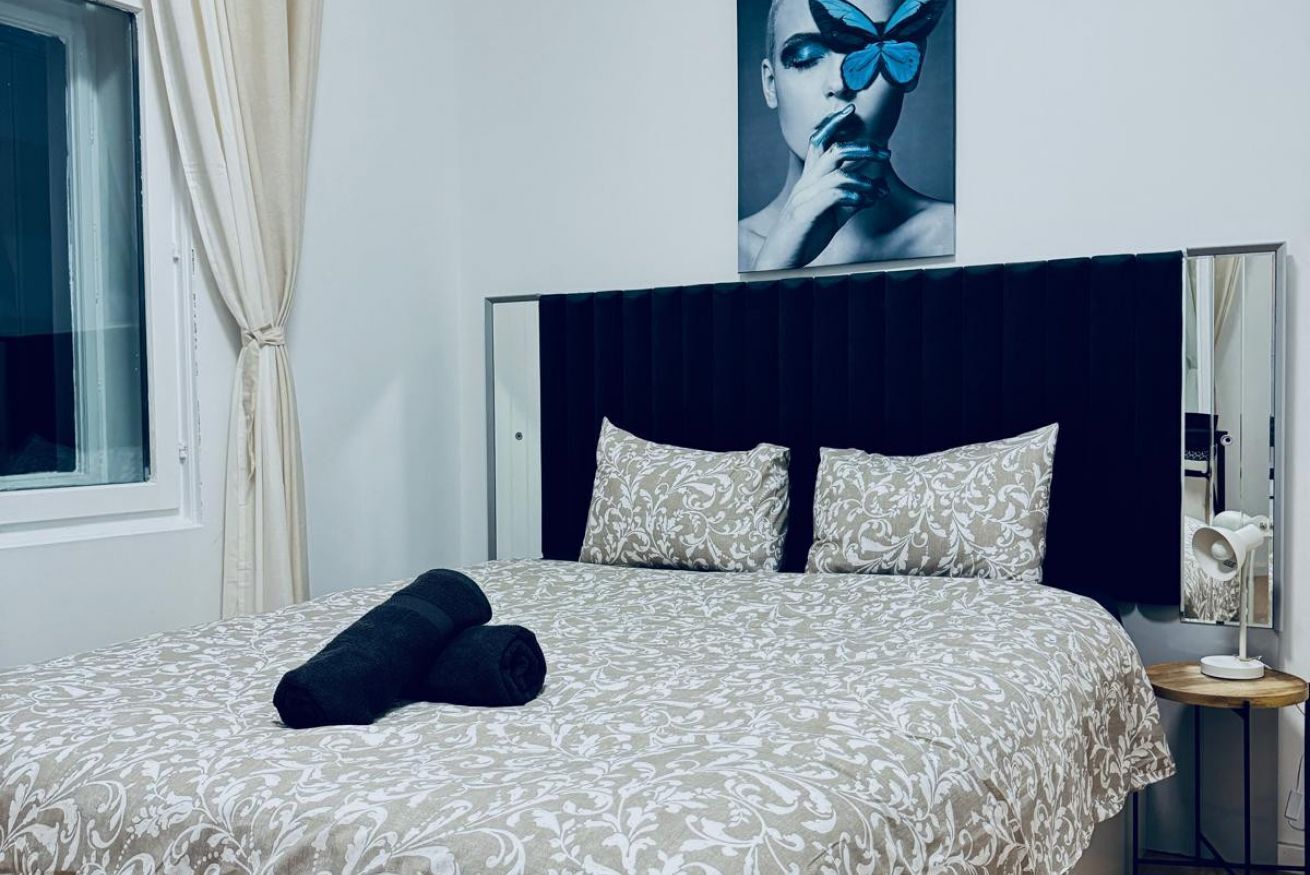 Un lit bien fait, avec une literie à motifs, une tête de lit, une lampe de chevet et une fenêtre avec des rideaux.