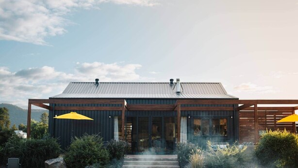 A modern building with a metal roof, large windows, and a wooden deck.