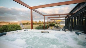 A hot tub with a wooden pergola structure, surrounded by a landscaped garden and a view of distant hills.