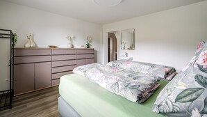 A bedroom with a bed, dresser, mirror, and a small bathroom with a sink. - Waldrose Apartment with Mountain View, Private Terrace, and Wi-Fi (Oberharmersbach)