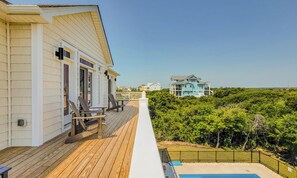 En træterrasse med udendørs møbler, en swimmingpool og udsigt til et stort hus i baggrunden.