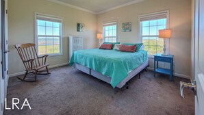 A bedroom with a bed, rocking chair, two bedside tables, and a view of the outdoors.