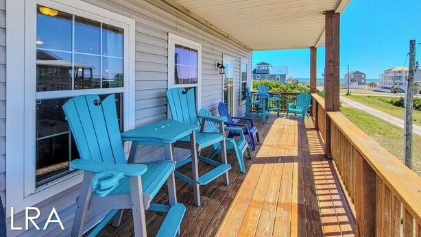 A covered porch with blue Adirondack chairs and a wooden deck.