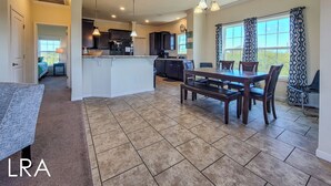 A spacious kitchen with a central island, dining table, and chairs. There is a separate dining area with a window and curtains.