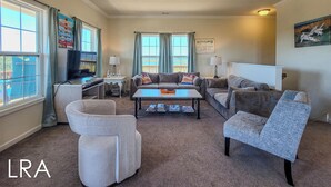A spacious living room with a large window, a flat-screen TV, a coffee table, and multiple seating options including a sofa and armchairs.