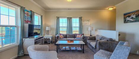 A spacious living room with a large window, a flat-screen TV, a coffee table, and multiple seating options including a sofa and armchairs.