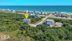 An aerial view of a coastal residential area with houses, a clear blue sky, and the ocean in the background.