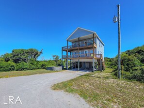 A two-story building with a balcony on the upper floor, a driveway leading to the entrance, and a utility pole to the right. - Sound Escape-NEW!-Stunning Sound Views! (North Topsail Beach)