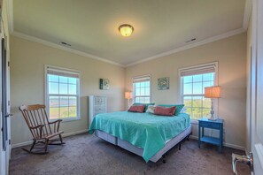 A bedroom with a bed, rocking chair, two bedside tables, and a view of the outdoors. - Sound Escape-NEW!-Stunning Sound Views! (North Topsail Beach)