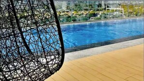 Una silla colgante junto a una piscina con vistas a una zona residencial y colinas.