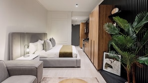 Un dormitorio moderno con una cama, mesita de noche y velador. Hay una planta y un cuadro en la pared.