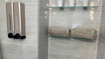 A bathroom with a glass shower enclosure, a towel rack, and three potted plants on a shelf.