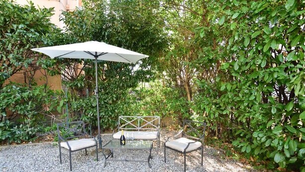 A patio with a metal table and two chairs, a white umbrella, and a bottle of wine. - AS VILLARTE (Agliana)