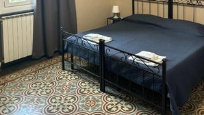A bedroom with a bed, a radiator, a window with curtains, a lamp, and a painting on the wall. - AS VILLARTE (Agliana)