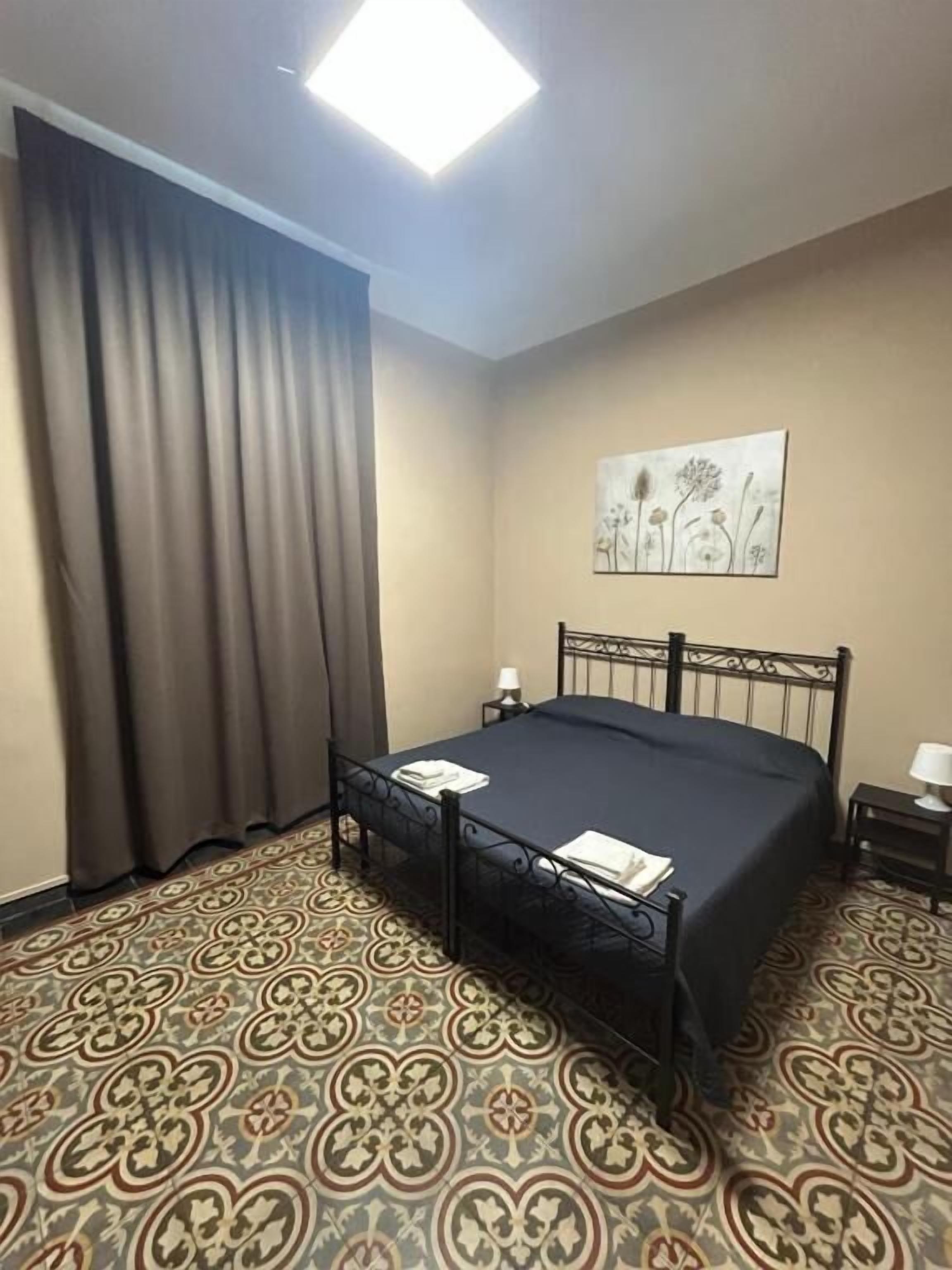 A hotel room with a bed, a nightstand, a lamp, a painting on the wall, and patterned carpet.