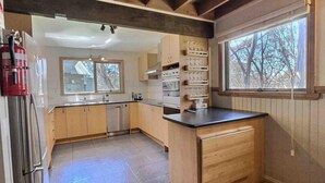 Eine Küche mit Holzschränken, einem Edelstahlkühlschrank, einem Doppelbackofen und einem Fenster mit Blick auf Bäume.