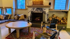 Ein gemütliches Wohnzimmer mit Kamin, einer Couch mit Kissen, einem runden Couchtisch und einem Sessel.