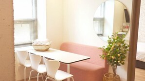 A small room with a white table, four white chairs, a pink sofa, a round mirror, and a wicker basket.