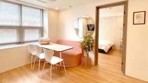 A modern room with a dining table, chairs, a pink sofa, a small plant, a bed, and a mirror.