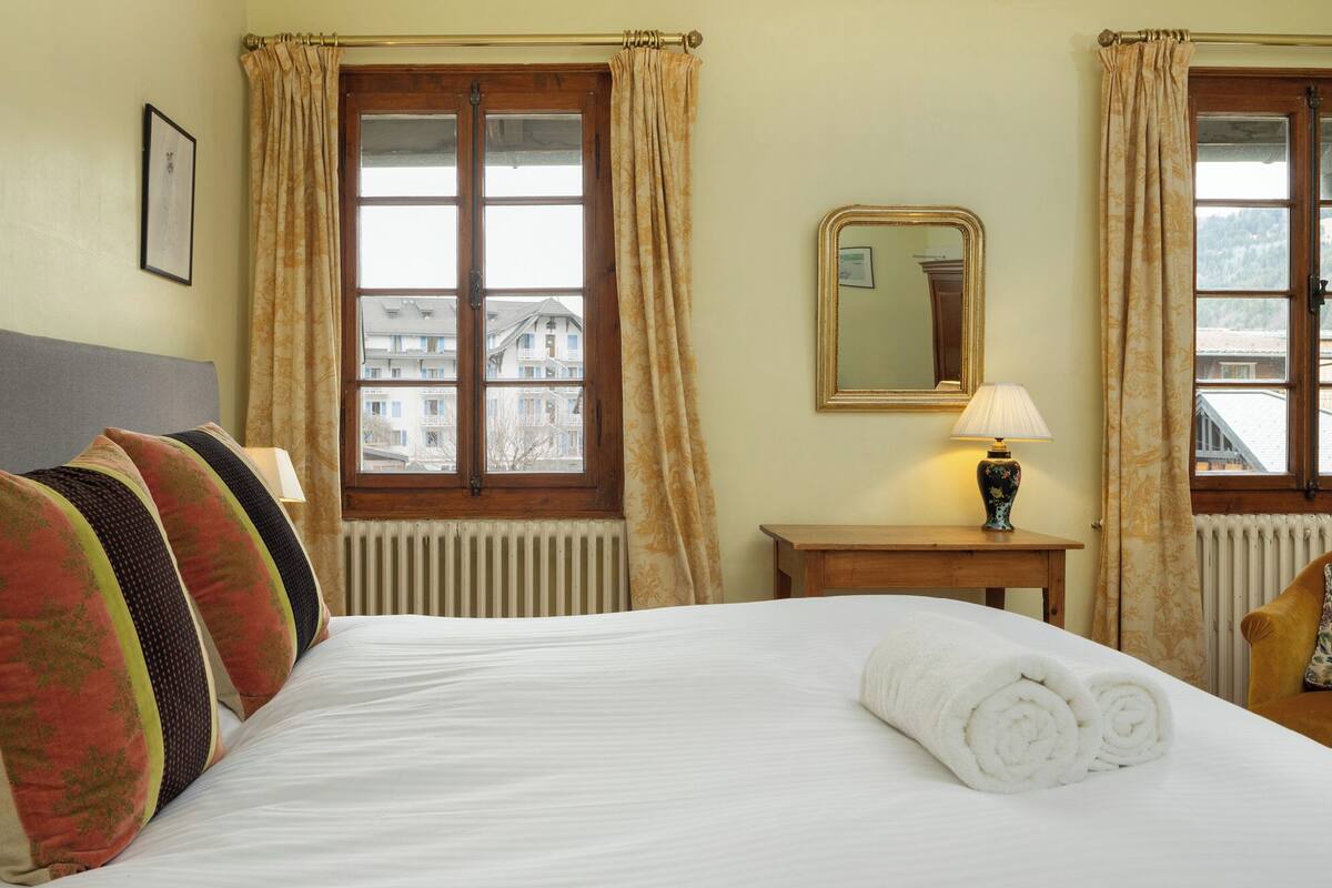 Una camera d'albergo con un letto grande, una testiera in legno, un comodino con una lampada e una finestra con tende.