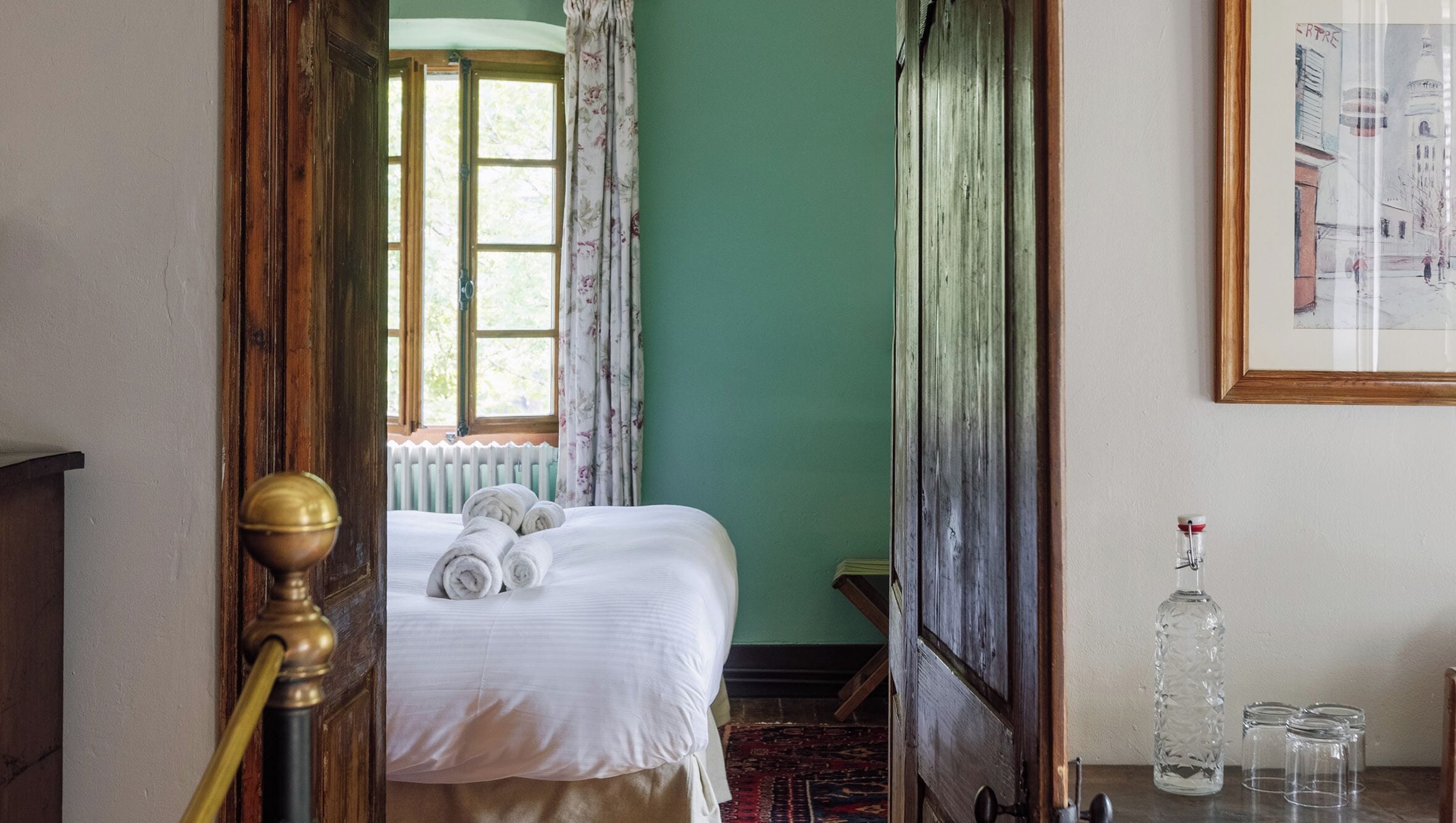 A room with a bed, a radiator, a window with curtains, and a framed picture on the wall.