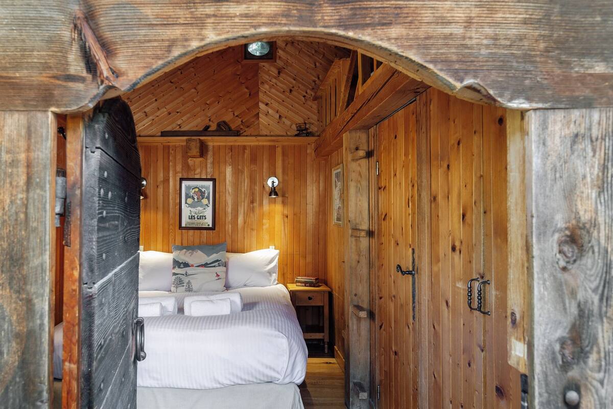 Un interno in legno con un letto, un tavolino e un lampadario a parete.