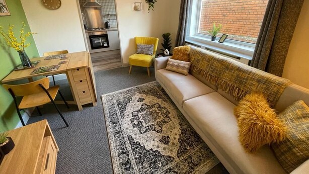 Ein gemütliches Wohnzimmer mit einer Couch, einem Esstisch und einer durch eine offene Tür einsehbarer Küchenbereich.