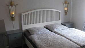 Une chambre à coucher avec une tête de lit blanche, deux tables de chevet, une couvre-lit à motifs et des lampes fixées au mur.