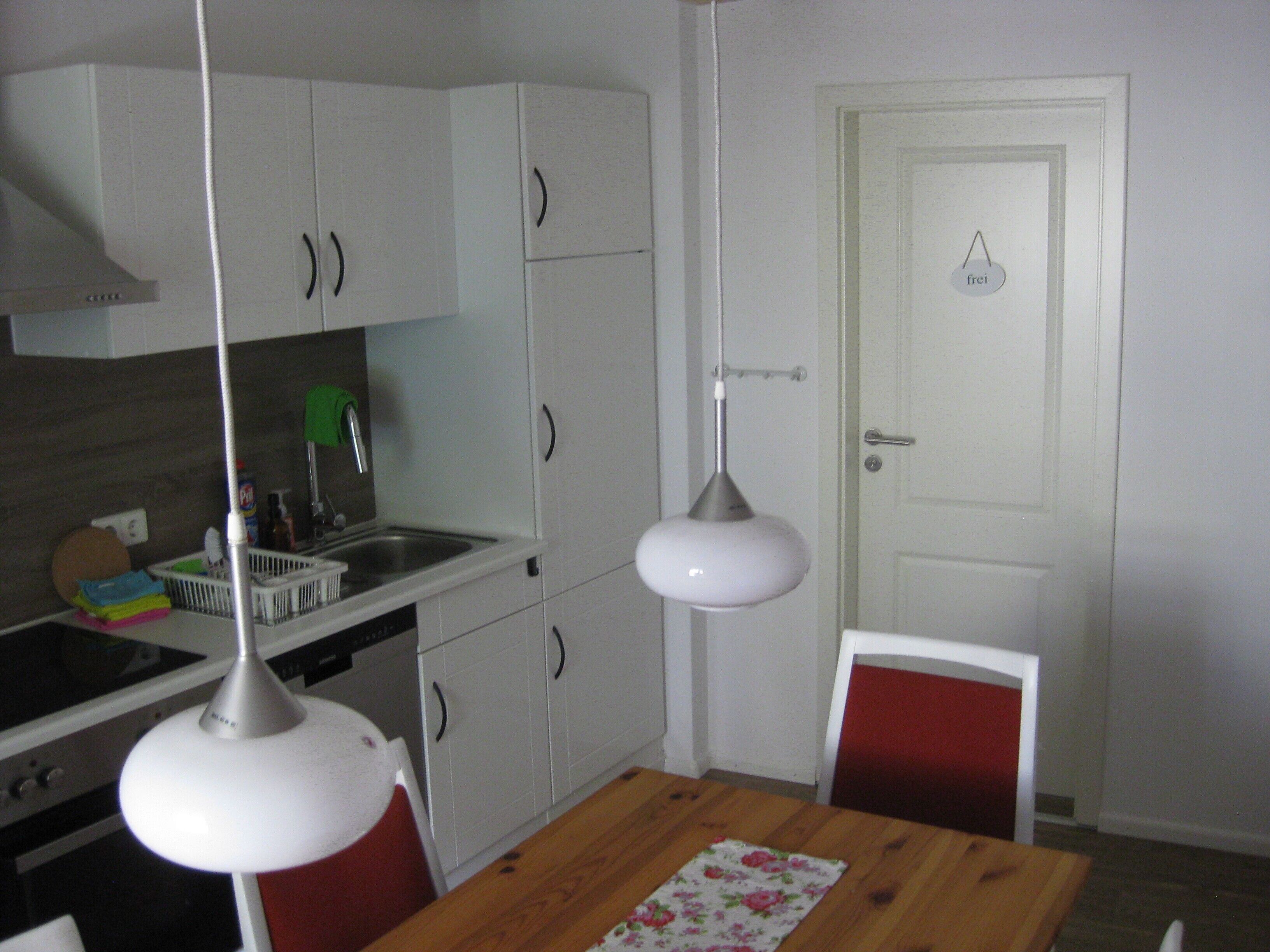 A compact kitchen with white cabinets, a wooden dining table, and a red chair.