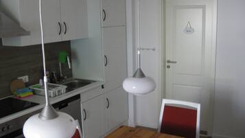 A compact kitchen with white cabinets, a wooden dining table, and a red chair.