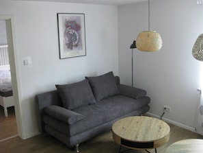 Ein graues Sofa, ein runder Tisch, eine hängende Leuchte und ein gerahmtes Kunstwerk an der Wand.
