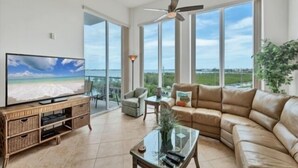 A spacious living room with a large TV, leather sofa, and a balcony with a view of the beach. - Sunset Views, Sand Between Your Toes-Your Winter Escape Awaits! (Englewood)