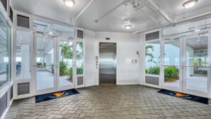 A modern elevator area with glass doors, a tiled floor, and ceiling pipes. - Sunset Views, Sand Between Your Toes-Your Winter Escape Awaits! (Englewood)
