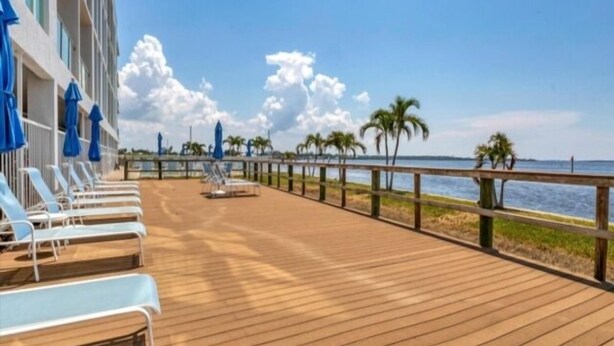 A wooden deck with lounge chairs and umbrellas, a wooden railing, and a view of the sea with palm trees. - Sunset Views, Sand Between Your Toes-Your Winter Escape Awaits! (Englewood)